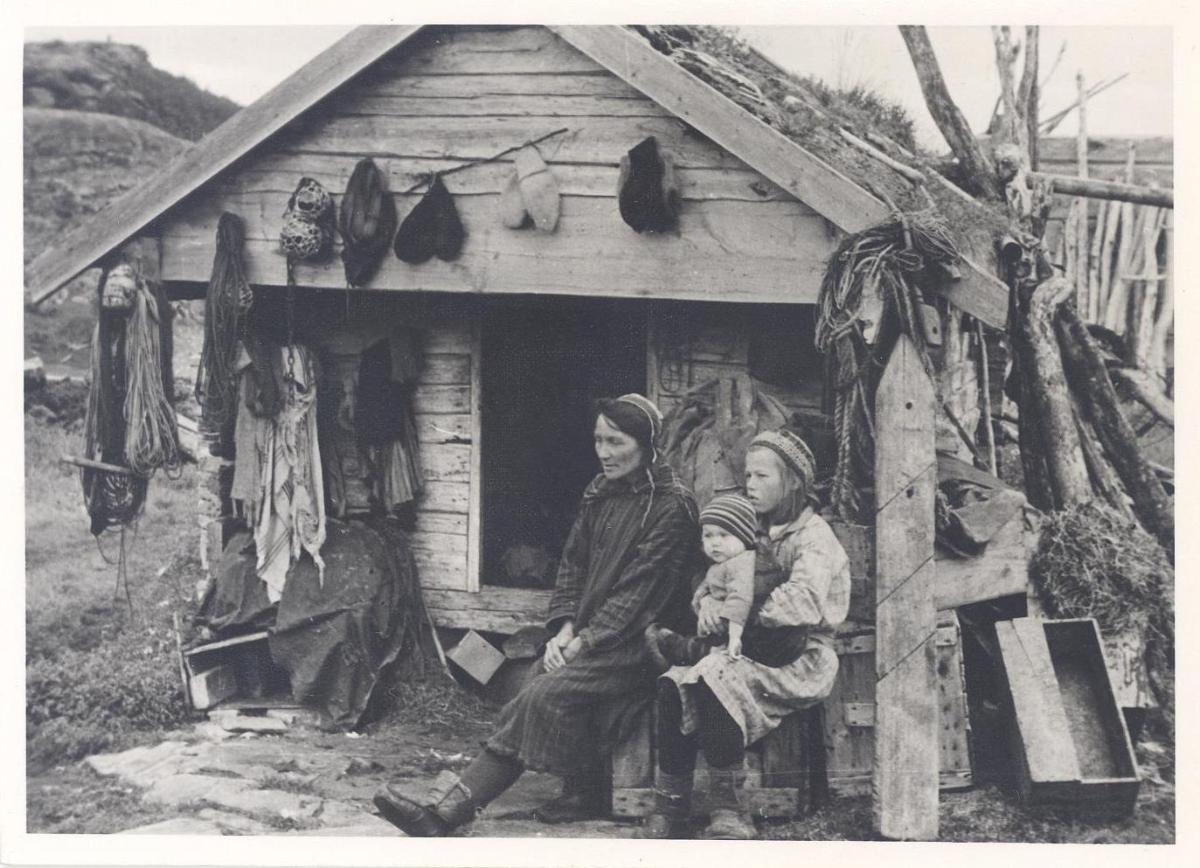 Samin mit zwei Kindern vor Holzhaus