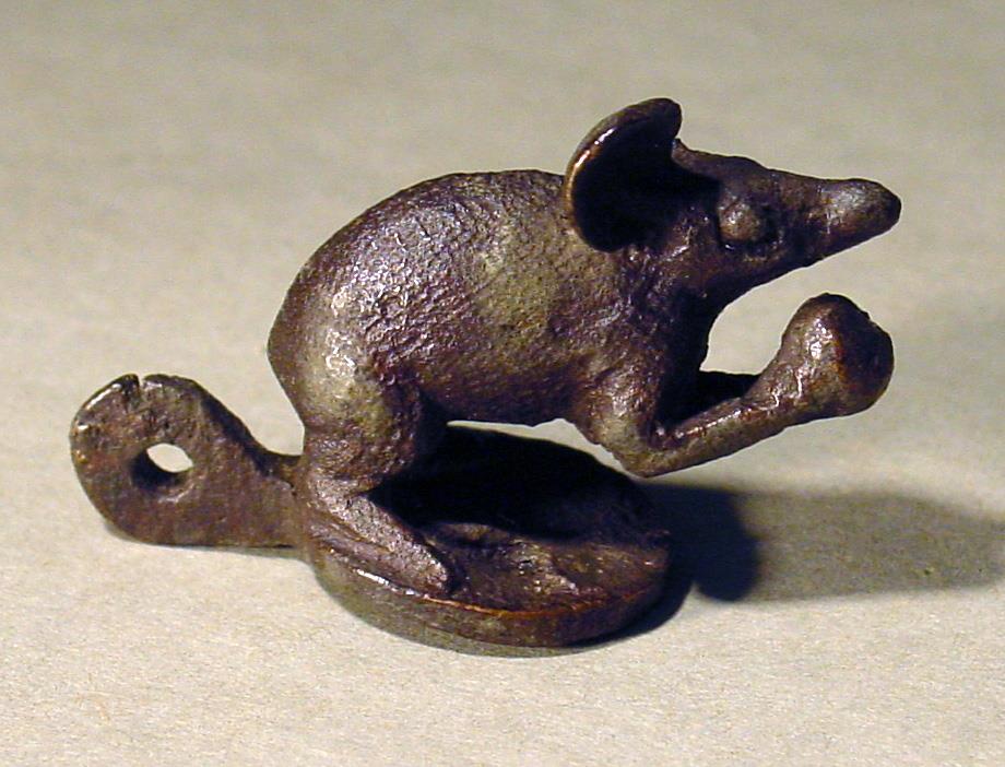 Statuette einer Maus, mit den Vorderbeinen eine Frucht haltend, das linke Ohr abgebrochen, an der Basis hinten eine Öse (Lampendeckel)
