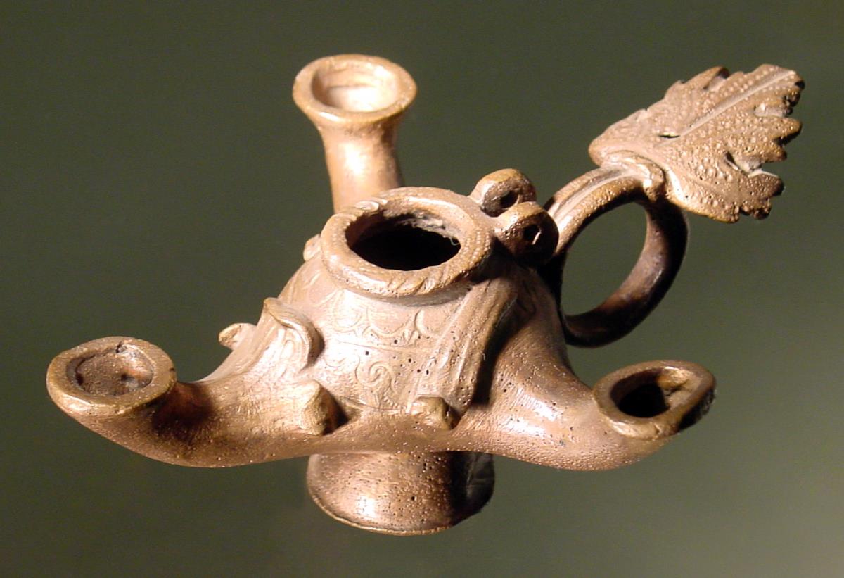 Lampe mit drei Tüllen. Eingußloch war mit einem zwischen zwei Ösen beweglichen Deckelchen, das jetzt fehlt, verschlossen. Konischer Fuß