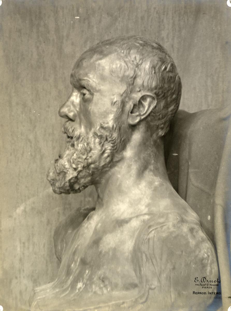 Die Büste Jean-Paul Laurens vor der fleckigen Mauer im Atelier du Dépôt des marbres, hinter der Büste eine Stoffdraperie
