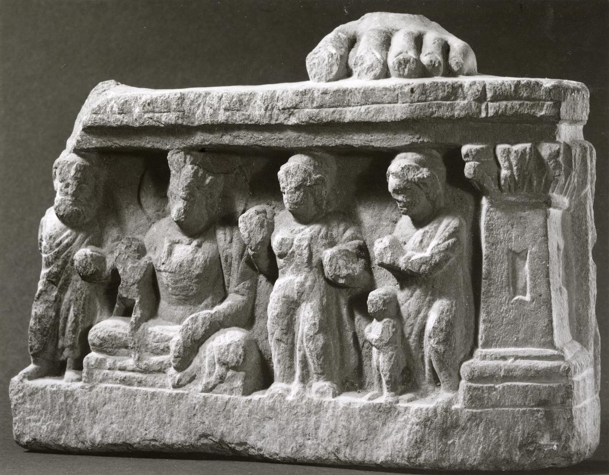 Fuß eines stehenden Buddha (Fragment). Sockelrelief: Verehrungsszene mit sitzendem zukünftigen Buddha Maitreya in Schutzgeste (abhaya-mudra)