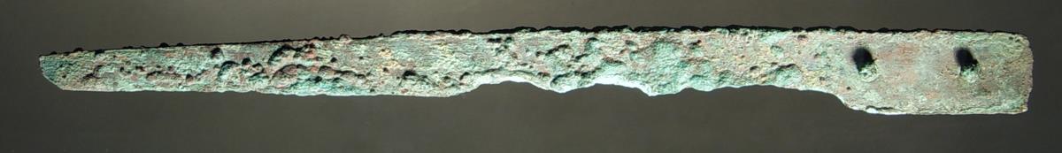 Einschneidiges Messer. Der Rücken scheint eine Strecke weit mit regelmäßigen Kerben zur Verzierung versehen zu sein. Schneide teilweise durch die Patina zerfressen