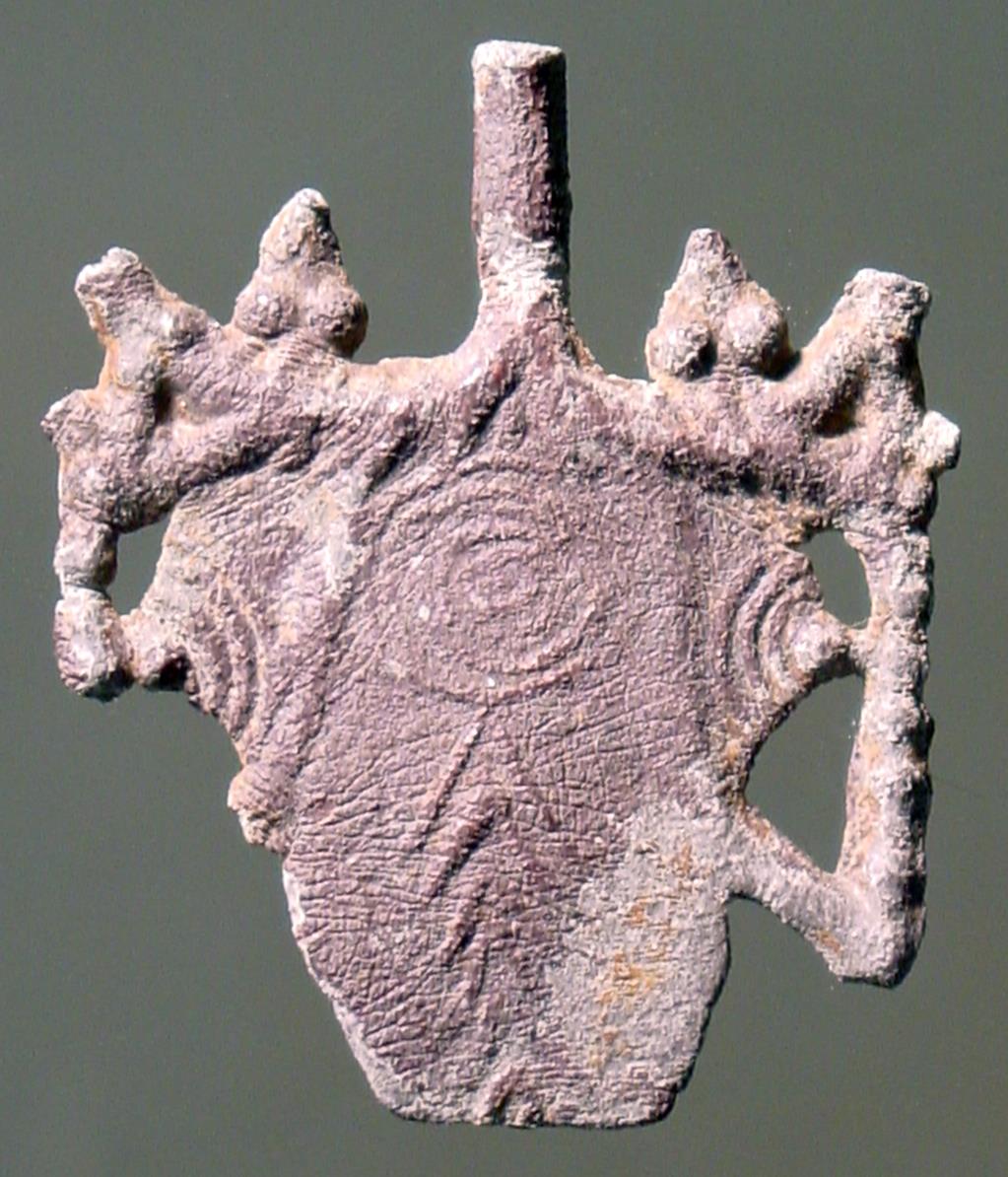 Mit Wollbinden geschmückter Stierkopf en face; über der Stirn hat sich noch der Ansatz vom Stiel eines Doppelbeils (?) erhalten, Rückseite mit Blattrippen verziert