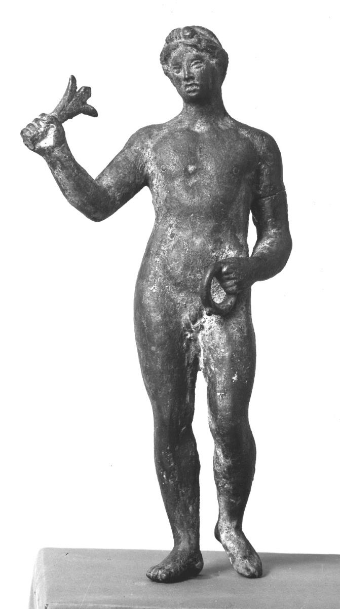 Statuette eines nackten Jünglings, auf dem Kopfe über der Stirn eine Haarschleife (?), in der erhobenen L. und der ein wenig vorgestreckten R. je ein Rest eines unbestimmbaren Gegenstandes (Attributs)