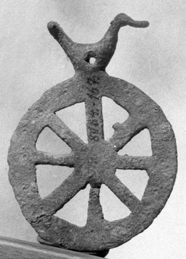 Kleines Rädchen, oben mit primitivem Vogel, der horizontal durchbohrt. Auf dem Rande und im Mittelpunkt kleine Kreise mit Zentralpunkt einge(preß)t, auf beiden Seiten