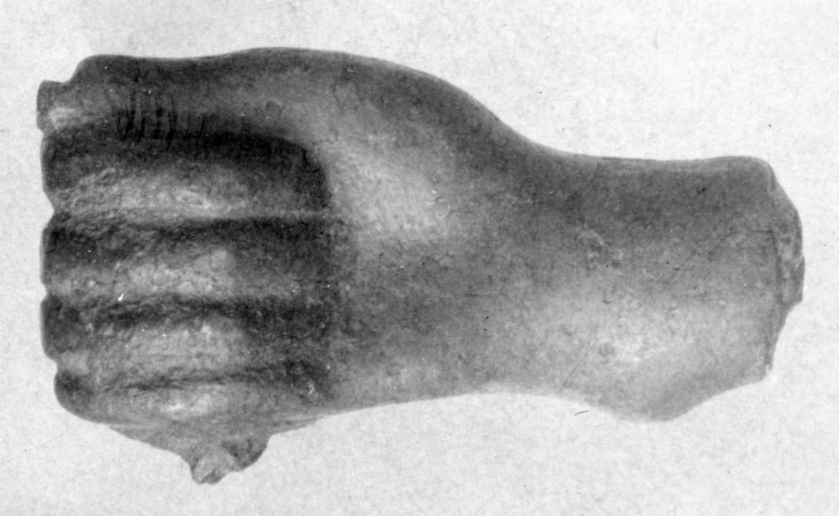 Hand von einer archaischen Statuette. Die Faust ist geballt, darin Reste von einem eisernen Gegenstand