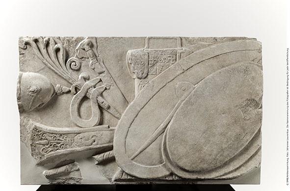 Brüstungsrelief (Waffenrelief) der Hallen des Athenaheiligtums in Pergamon. Linker Teil einer vollständigen, aus zwei Teilen bestehenden Brüstungsplatte: zwei Schilde vor größerem ovalen (gallischen) Schild; dahinter ein Panzer mit pflanzlichem und geometrischem Dekor, ein Langschwert und ein Helm sowie ein Steuerruder, mit pflanzlichem Dekor und einem Seeungeheuer verziert