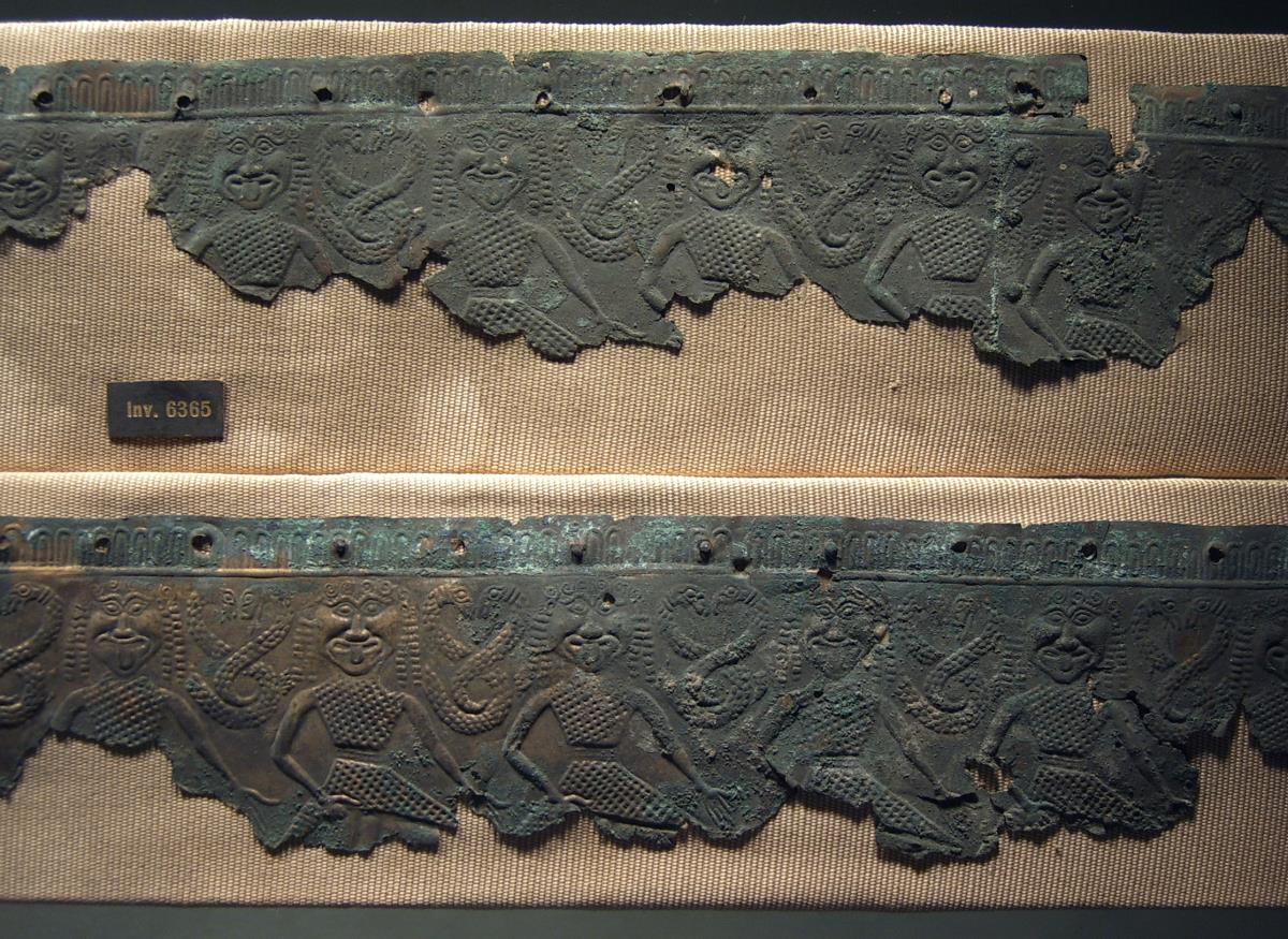 "Zwei dünne Bronzestreifen, zum Aufnähen auf die Kleidung oder Rüstung bestimmt, ..., sehr altertümlich" (Gürtel aus dünnem Blech mit Gorgonenfries)