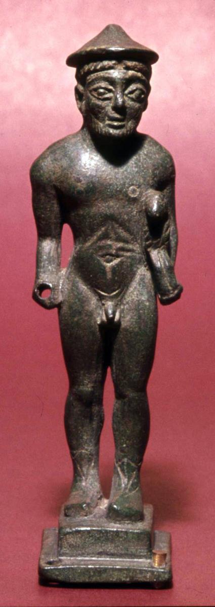 Archaische Votivstatuette eines nackten bärtigen Mannes mit Hut und Schnabelschuhen, einen kleinen Widder unter dem linken Arm tragend