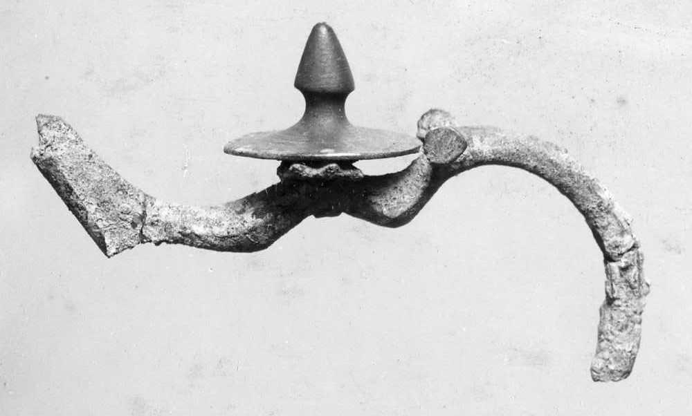 Fibel; die Nadel und die Bettung fehlen. Auf dem Bügel, der wie bei Misc. 6326, A 26ff. gebildet ist, ist ein großer Knopf mit Spitze als Verzierung aufgesetzt