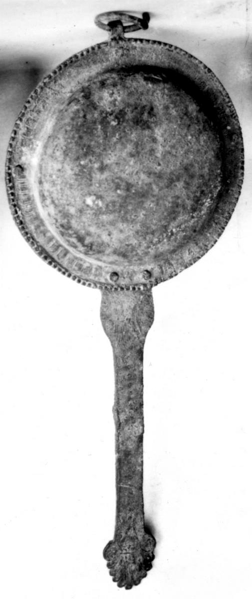 Klapper. Der lange Stiel endet unten in einer strengen Palmette. Der obere Teil besteht aus zwei aufeinander gestülpten zusammengenieteten flachen Schalen, darin zwei Bronzekügelchen, an dem Gerät ein Ring zum Aufhängen