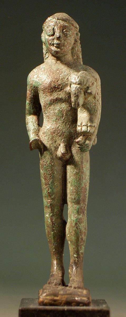 Archaische Votivstatuette eines nackten Jünglings mit Hut, einen kleinen Widder unter dem linken Arm tragend