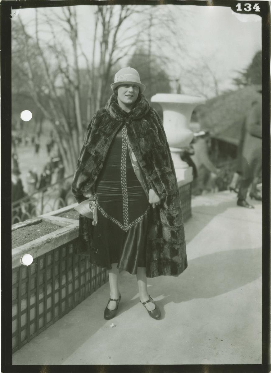 Frau in Kleid und Cape auf dem Rennplatz