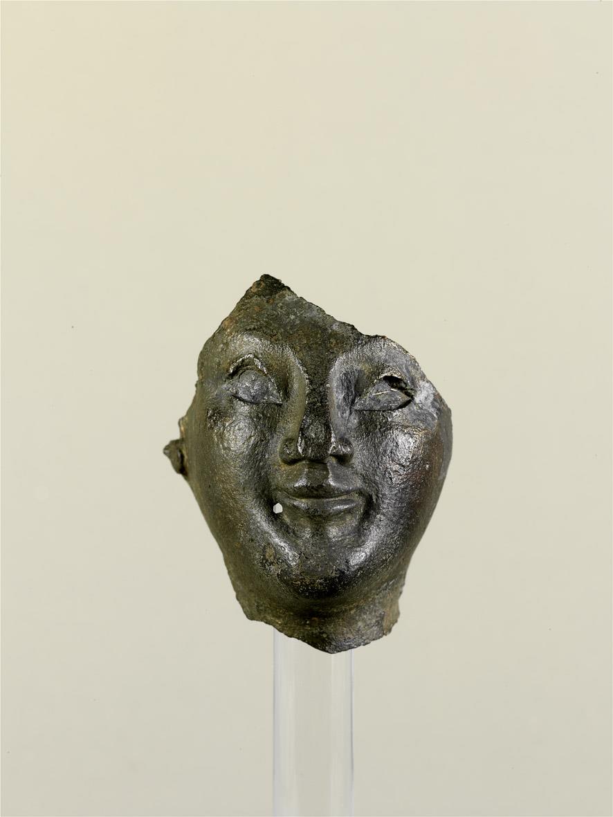 Fragment eines Kopfes, Gesicht, Teile vom Hals, Stirn und rechtem Ohr, Loch unterhalb des rechten Mundwinkels, Nase eingedrückt, Hohlguss, Augen waren eingelegt