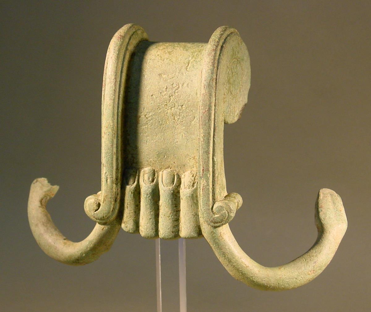 Kesselhenkel, das Mittelstück als Hand, die Seitenauflager als Schlangen gebildet (= Henkel eines archaischen Volutenkraters)