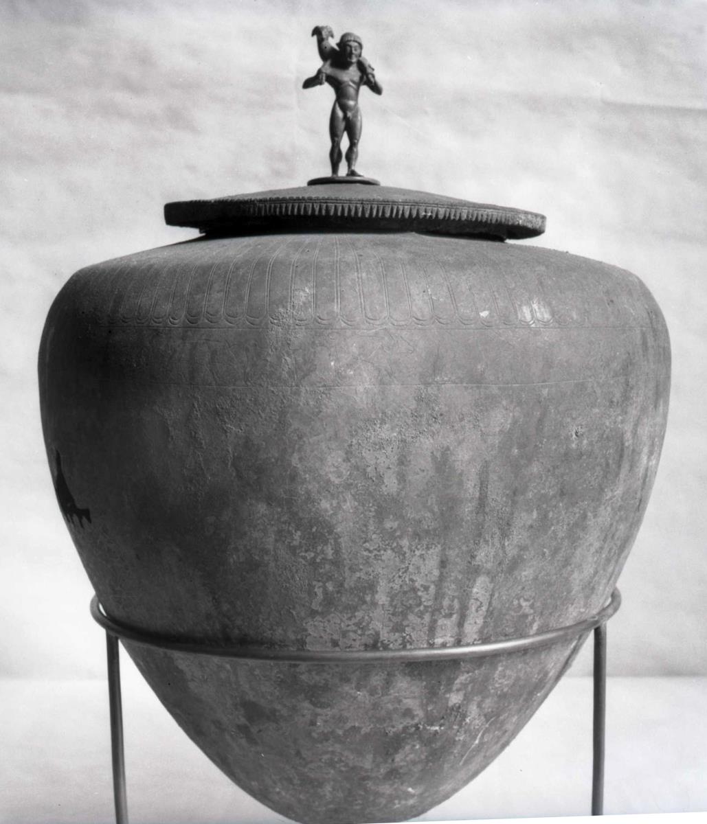 "Deckelgefäß mit eingeritzten Ornamenten und Figurenfries" ..."auf dem Deckel die Figur eine widdertragenden Hermes" (Urne mit Statuette eines Widderträgers auf dem Deckel)