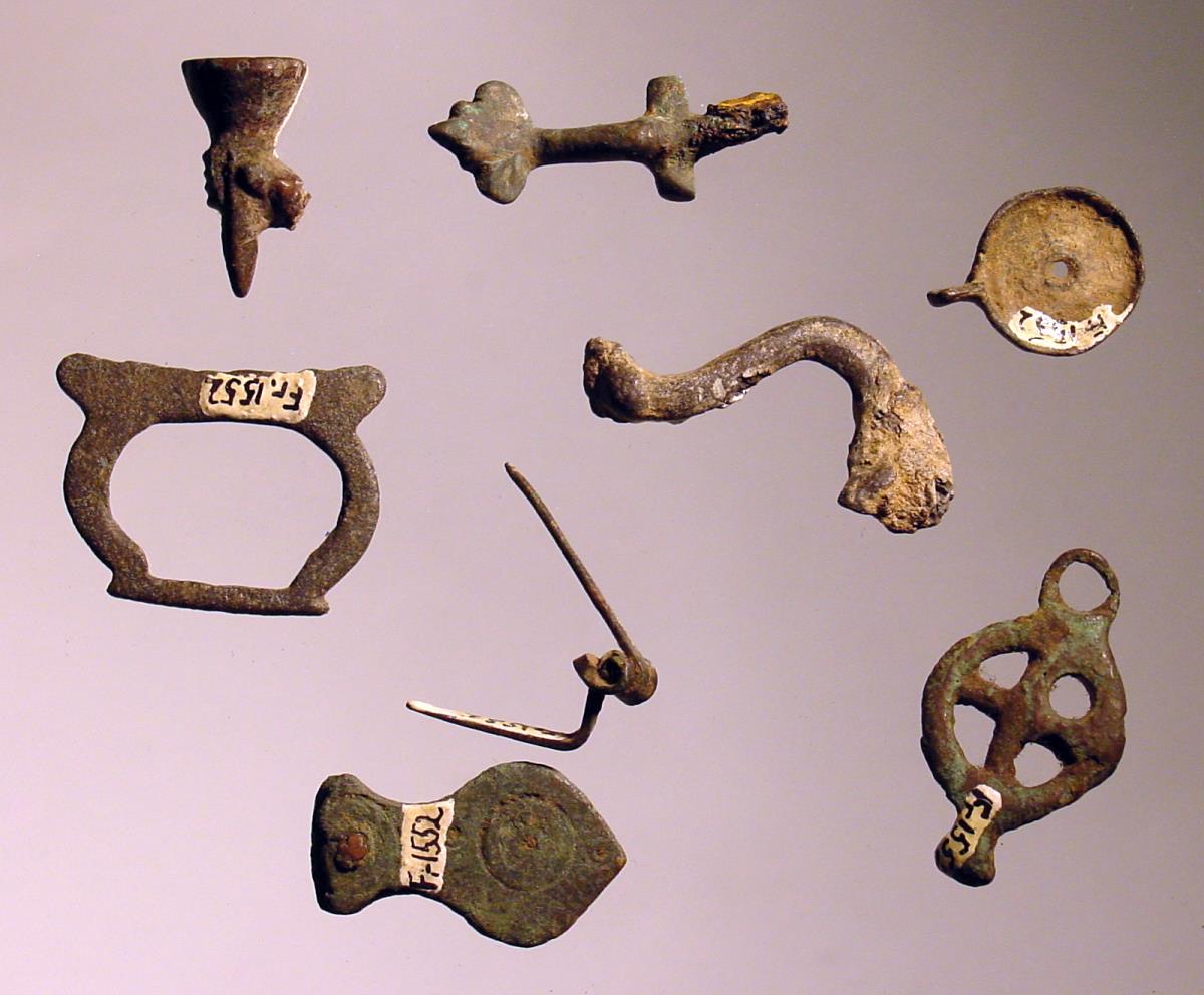 Neun verschiedene Teile: Hand mit Fackel, Mithrassymbol (?) in Form einer Säge, Teil einer Siegelkapsel, Miniaturhenkel, Fibelfragmente etc.