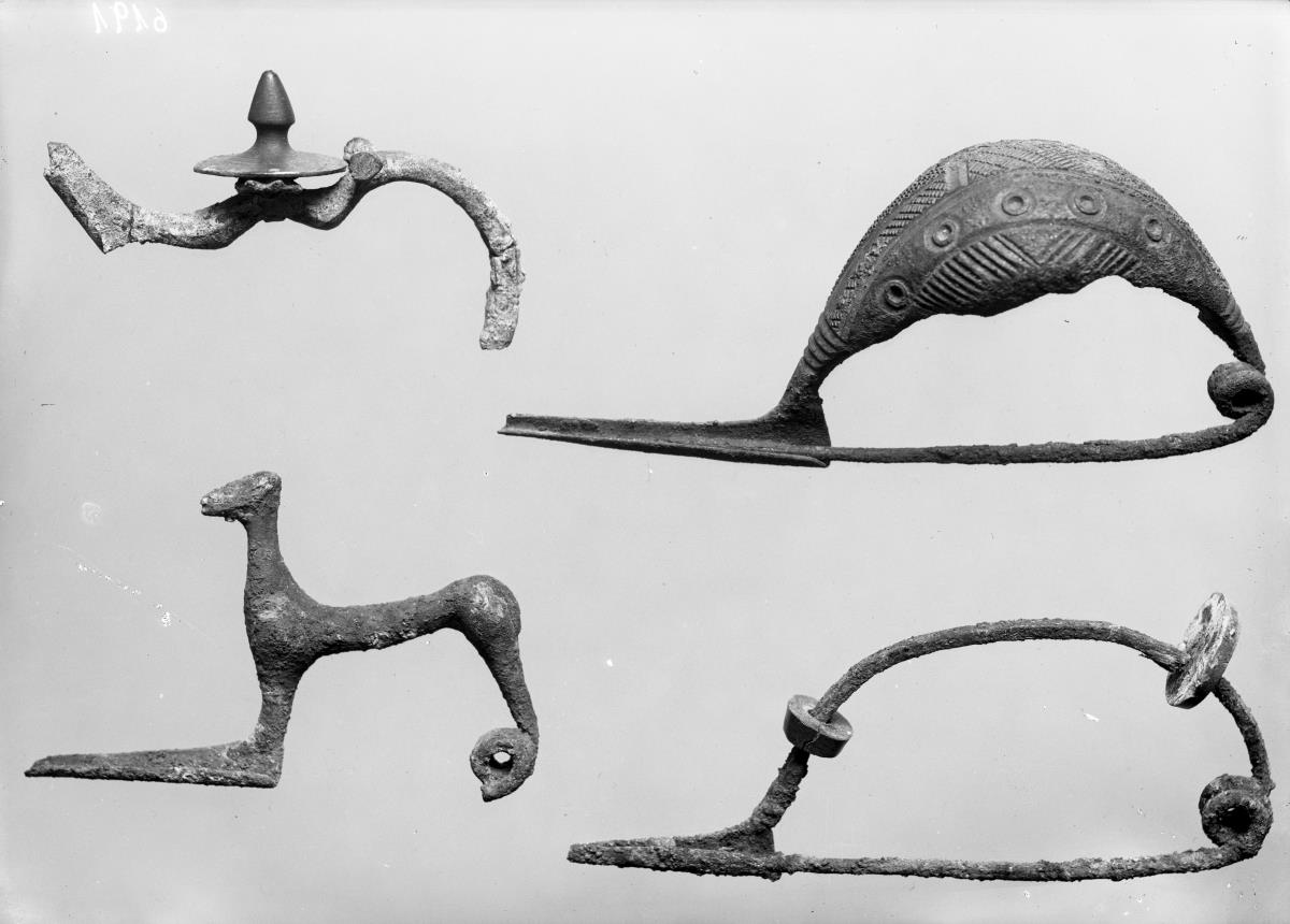 Große Fibel, vollständig erhalten; auf dem hohen breiten Bügel mit dem Bunzen eingefügte Verzierungen (Kreise und Linien)