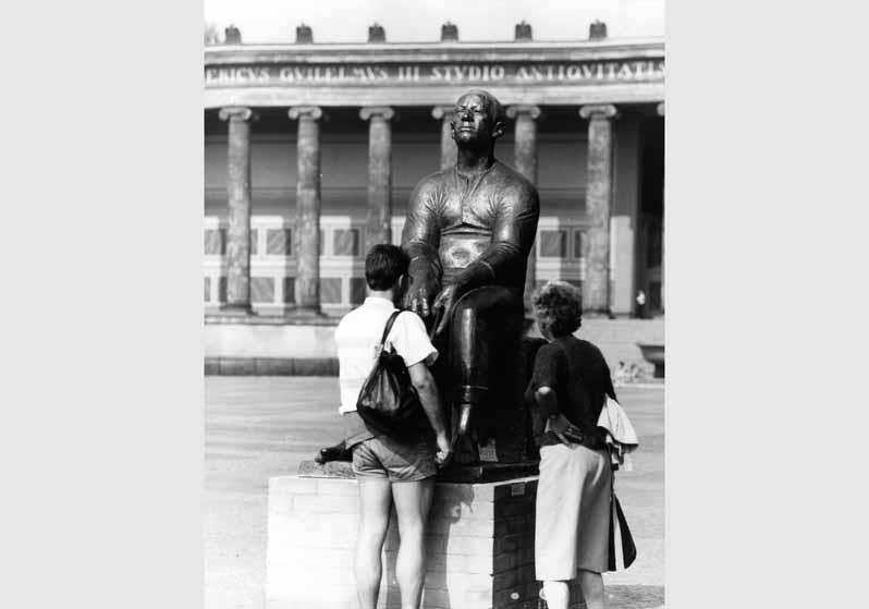 Personen vor der Skulptur "lesender Arbeiter" von Ludwig Engelhardt vor dem Hintergrund des Alten Museums