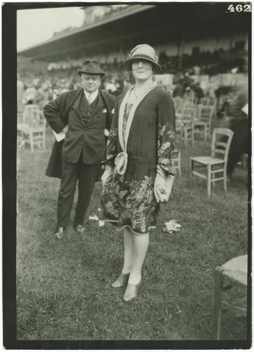 Frau in Ensemble und Mann in Anzug und Mantel auf dem Rennplatz in Chantilly