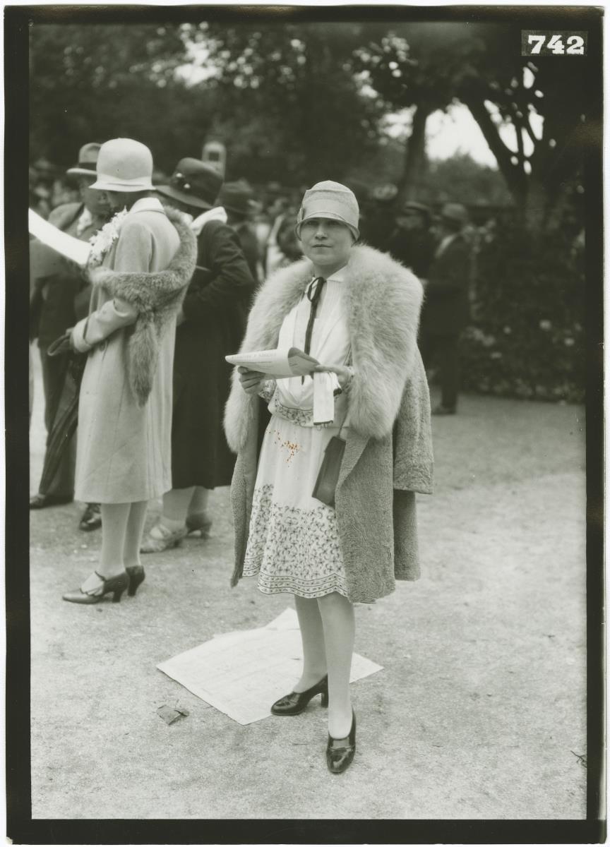 Frau in Kleid und Mantel auf dem Rennplatz in Deauville