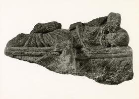 Erzählende Szene (Fragment): Unterkörper eines sitzenden Buddha (?) mit aufbäumendem Tier (?) im Sockel (links, erste Predigt?); sitzender Mönch (?) (rechts)