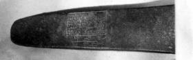 Altes Beil: Auf der einen Seite eingegraben zwei Fußsohlen, darin Zauberinschrift mit griechischen Buchstaben, und Oval, auch mit Zauberinschrift gefüllt, auf der anderen Seite rechteckiges Feld mit Zauberinschrift und daneben ein Zauberzeichen.