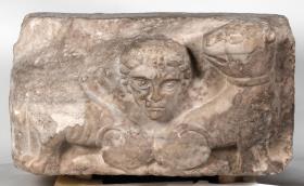 Kubisches Architekturelement mit Relief eines männlichen Kopfes zwischen zwei zurückblickenden Löwen
